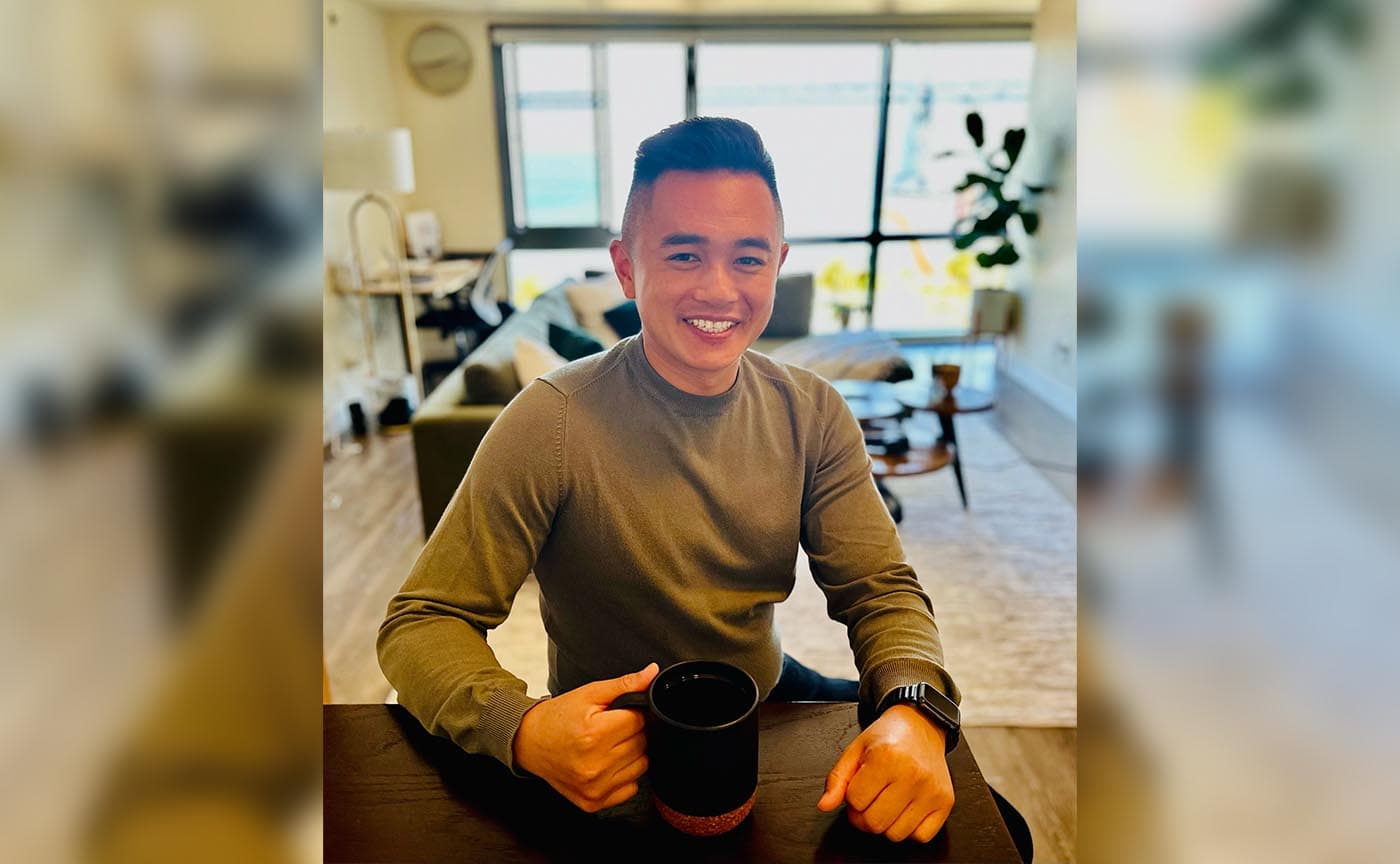 Andrew Ngin smiling at a table with a coffee mug