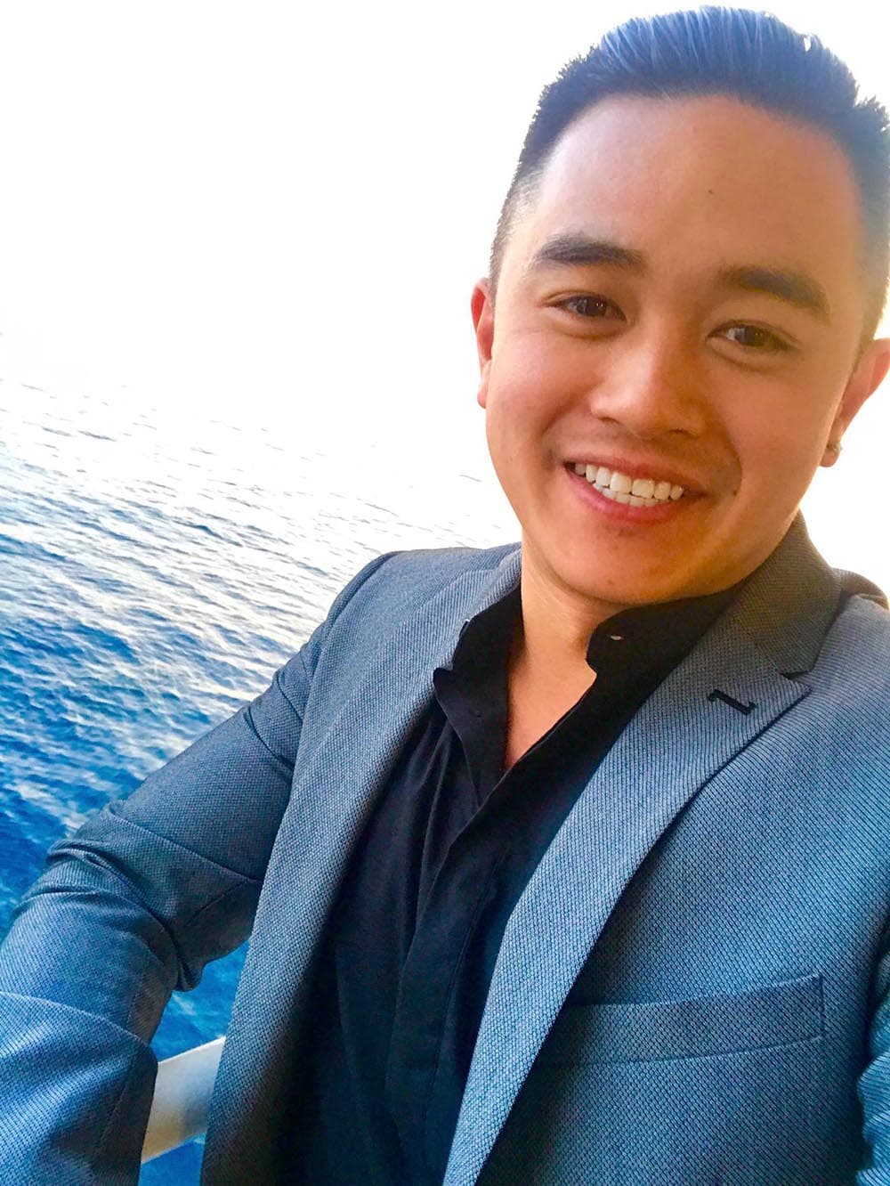 Andrew Ngin in a blazer on a cruise, ocean in the background